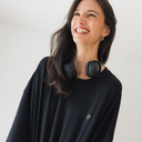 Frau die lacht und Kopfhörer um die Schultern hängen hat. Sie trägt das oversized shirt joy in der Farbe schwarz.
