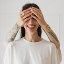 Frau die lacht, weil ihr die Augen zugehalten werden. Sie trägt das oversized shirt joy in der Farbe ecru (ungefärbte Baumwolle).