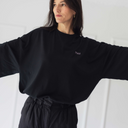 Frau mit ausgebreiteten Armen und stolzem Blick, die das oversized shirt trust in schwarz trägt.