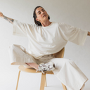 Frau sitzt entspannt am Stuhl und streckt ihre Arme. Sie trägt dabei das oversized shirt peace in der Farbe ecru (ungefärbte Baumwolle).