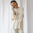 Frau entspannt vor einem Vorhang. Sie trägt dabei das oversized shirt peace in der Farbe ecru (ungefärbte Baumwolle).