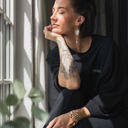Frau sitzt entspannt am Fenster und lässt sich von den Sonnenstrahlen wärmen. Sie trägt dabei das oversized shirt peace in der Farbe schwarz.