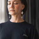 Frau sitzt entspannt am Fenster und lässt sich von den Sonnenstrahlen wärmen. Sie trägt dabei das oversized shirt peace in der Farbe schwarz.